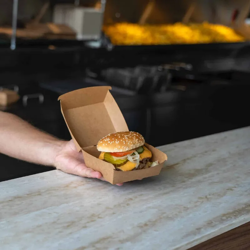 Cheeseburger in een open kraft bakje wordt aangereikt over de toonbank