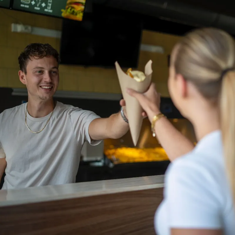 Medewerker overhandigt een puntzak verse friet over de toonbank