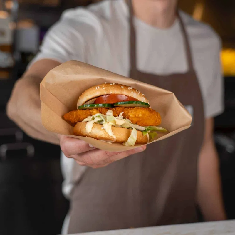 Medewerker toont een krokante kipburger in een papieren wikkel